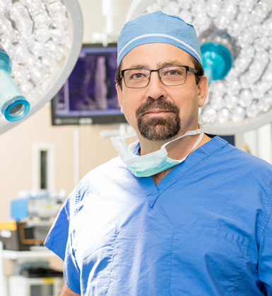 Doctor wearing scrubs, operating cap and surgical mask around neck standing in operating room