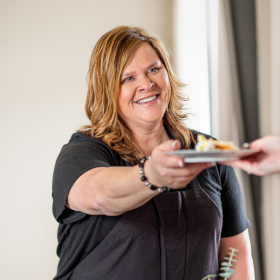 portrait photo: Linda smiling handing someone a plate of food