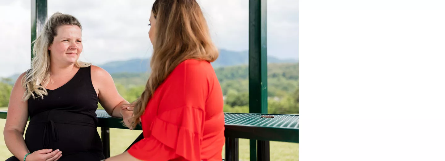 A woman speaking with a pregnant woman at a picnic table