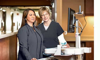 Two nurses in scrubs looking at a monitor